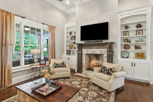 living area with built in shelves, dark wood-type flooring, a fireplace, ornamental molding, and a towering ceiling