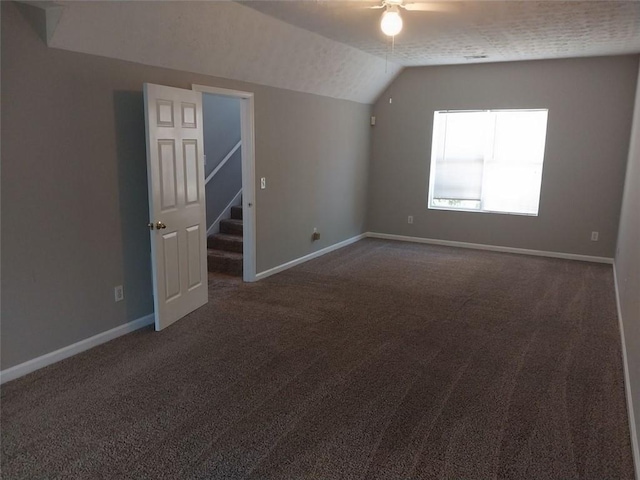 additional living space featuring dark colored carpet, a textured ceiling, vaulted ceiling, and ceiling fan