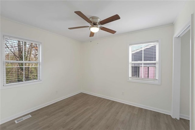 spare room featuring a wealth of natural light, visible vents, baseboards, and wood finished floors