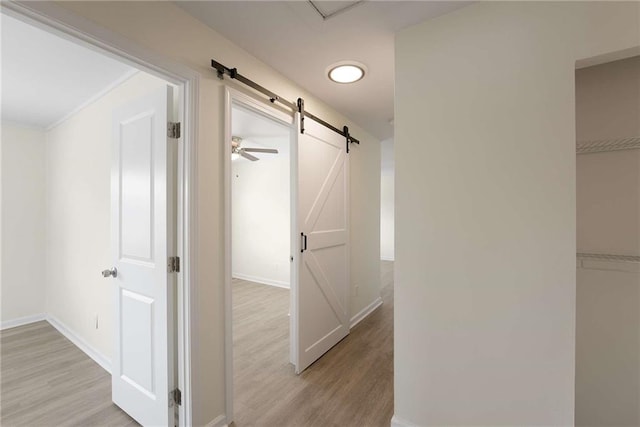 hallway featuring a barn door, baseboards, and light wood finished floors