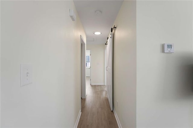 hall with a barn door, wood finished floors, and baseboards