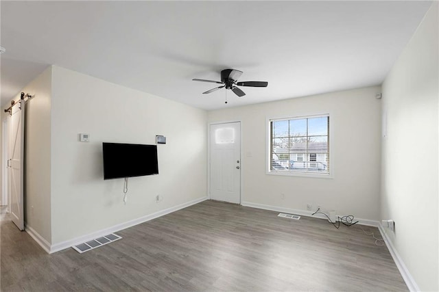 unfurnished living room featuring visible vents, ceiling fan, a barn door, and wood finished floors