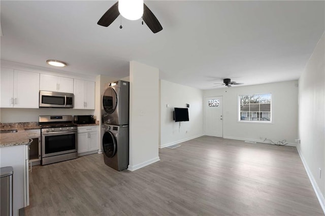 kitchen featuring light wood-type flooring, stacked washer and dryer, open floor plan, stainless steel appliances, and white cabinets