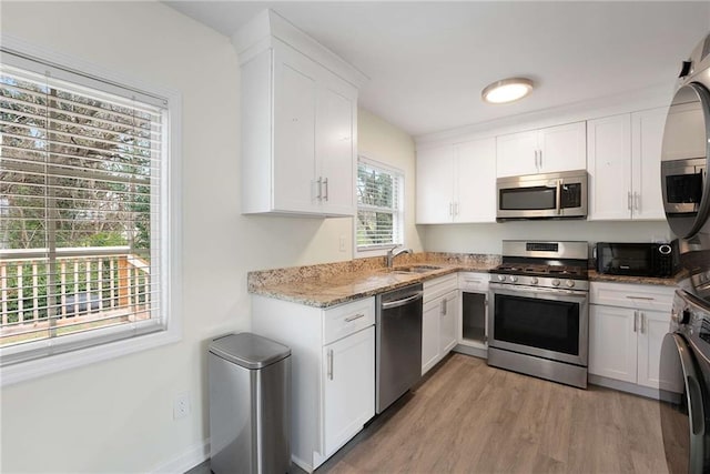 kitchen with light stone countertops, light wood-style flooring, a sink, appliances with stainless steel finishes, and white cabinetry