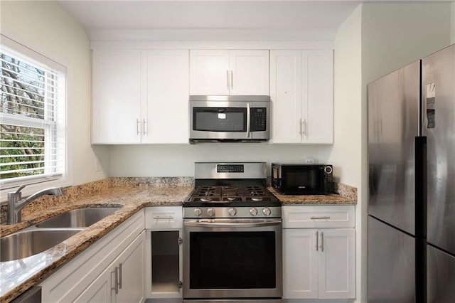 kitchen with white cabinetry, light stone counters, appliances with stainless steel finishes, and a sink