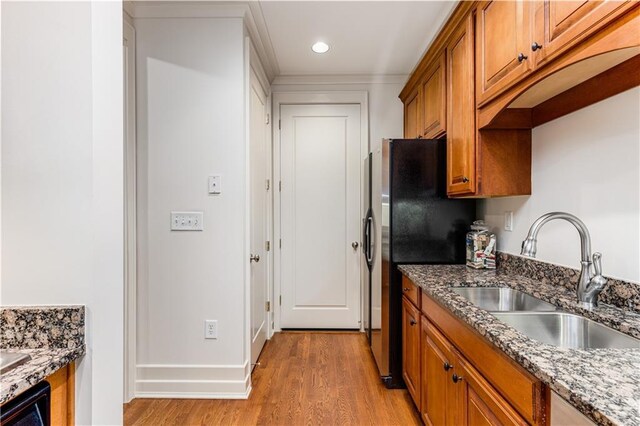 kitchen featuring brown cabinetry, light wood-style floors, dark stone counters, and a sink