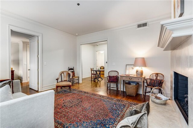 living area featuring a fireplace, wood finished floors, visible vents, baseboards, and ornamental molding