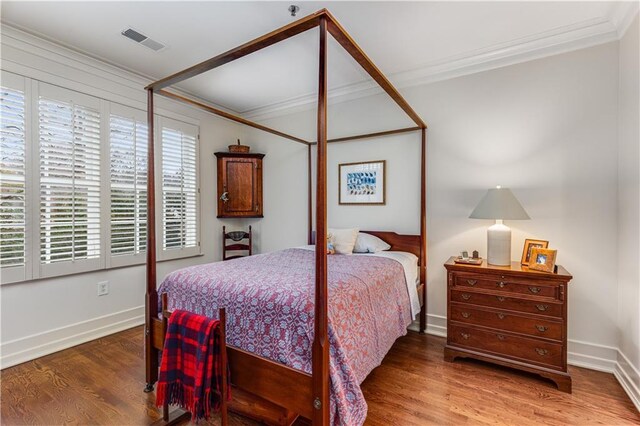 bedroom with visible vents, crown molding, baseboards, and wood finished floors