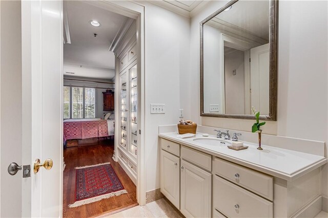 ensuite bathroom with ensuite bath, baseboards, wood finished floors, and vanity