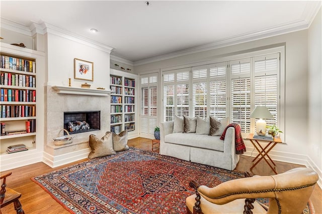 living area with built in shelves, ornamental molding, a high end fireplace, wood finished floors, and baseboards