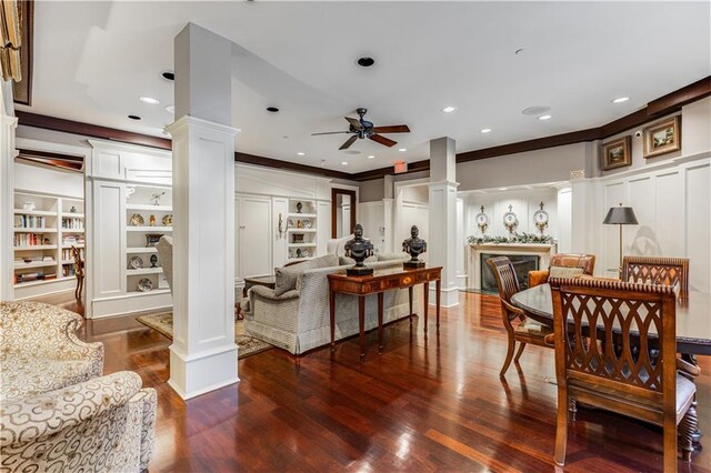 interior space featuring built in features, a decorative wall, a ceiling fan, wood finished floors, and ornate columns