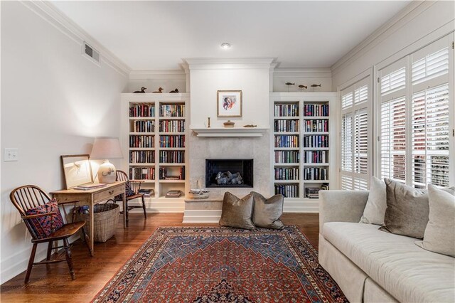 living area featuring built in shelves, crown molding, a fireplace, visible vents, and wood finished floors