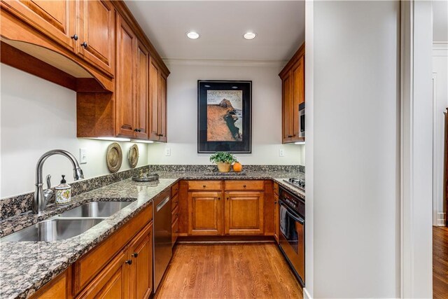 kitchen featuring brown cabinetry, light wood-style flooring, appliances with stainless steel finishes, dark stone countertops, and a sink