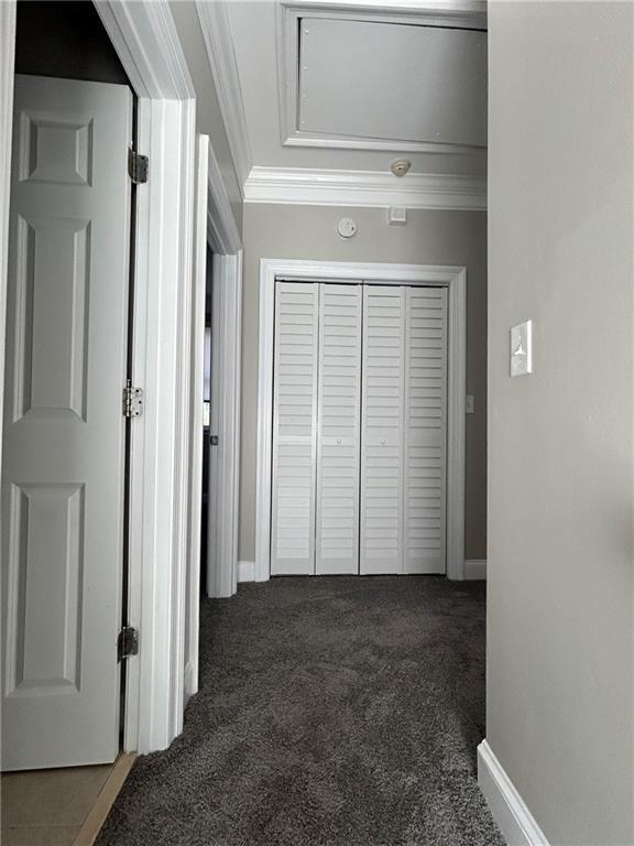 hallway with crown molding and dark colored carpet