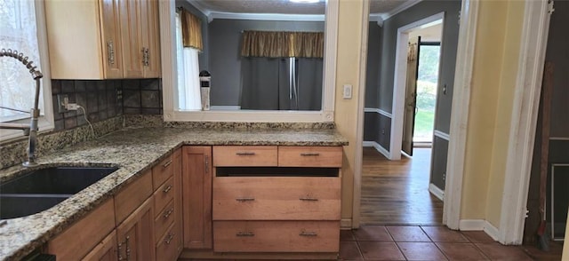 kitchen featuring tile patterned flooring, crown molding, sink, and light stone countertops