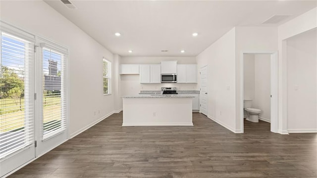 kitchen with dark hardwood / wood-style floors, white cabinets, a kitchen island with sink, light stone counters, and stainless steel appliances