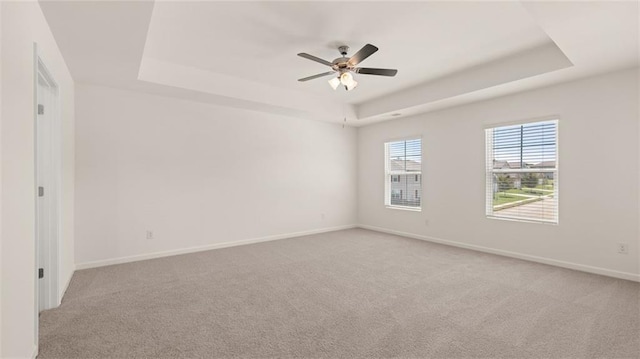 carpeted spare room featuring a raised ceiling and ceiling fan