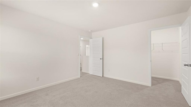 unfurnished bedroom with a walk in closet, a closet, and light carpet