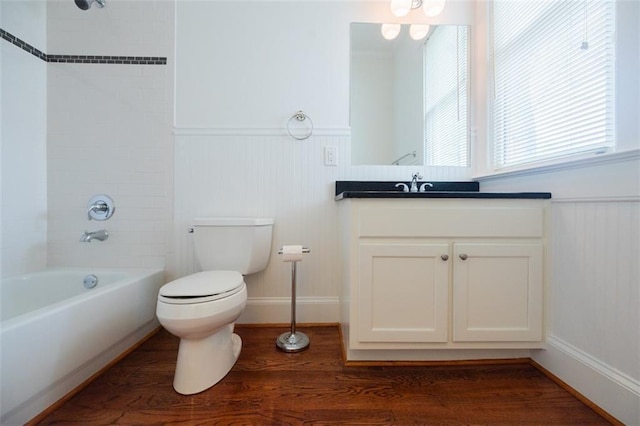 bathroom featuring a wainscoted wall, shower / washtub combination, toilet, wood finished floors, and vanity