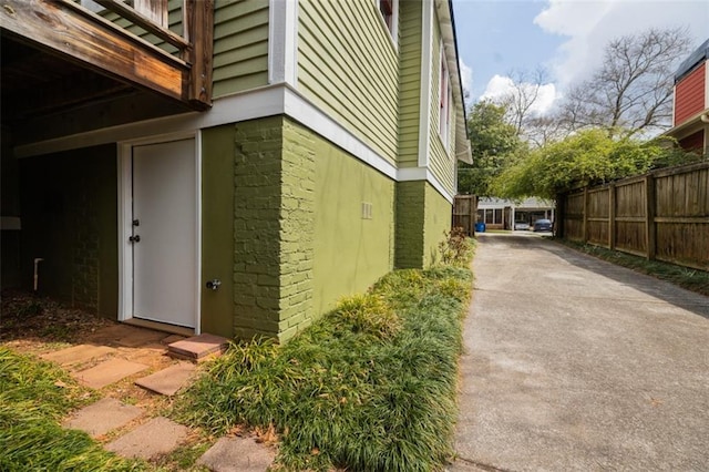 view of side of home with brick siding, driveway, and fence