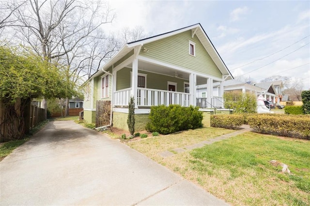 bungalow with ceiling fan, a front lawn, fence, covered porch, and driveway