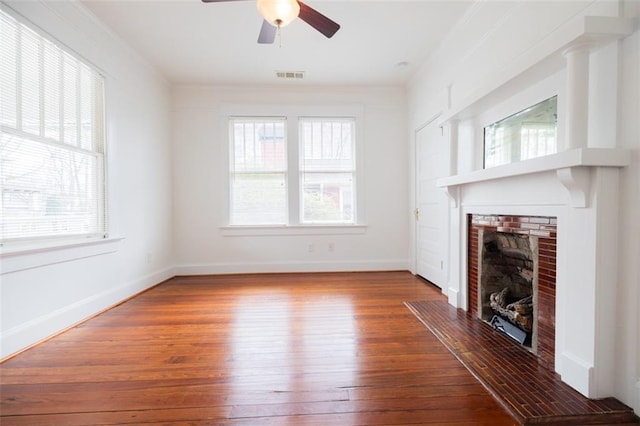 unfurnished living room with visible vents, ornamental molding, hardwood / wood-style floors, a brick fireplace, and ceiling fan