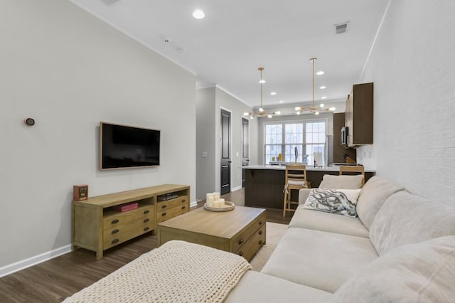 living room featuring dark wood-type flooring, ornamental molding, and a chandelier