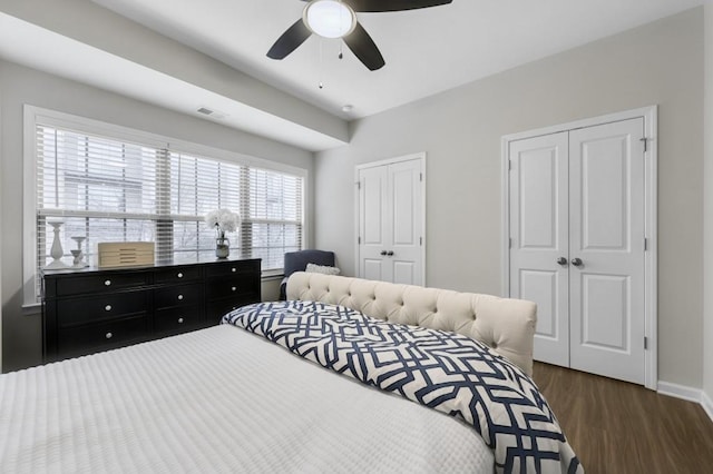 bedroom featuring two closets, dark hardwood / wood-style floors, and ceiling fan