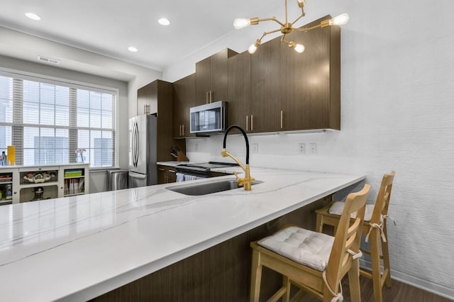 kitchen with appliances with stainless steel finishes, sink, dark hardwood / wood-style flooring, a kitchen bar, and light stone countertops