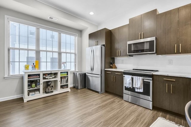 kitchen with appliances with stainless steel finishes, a wealth of natural light, and light hardwood / wood-style flooring