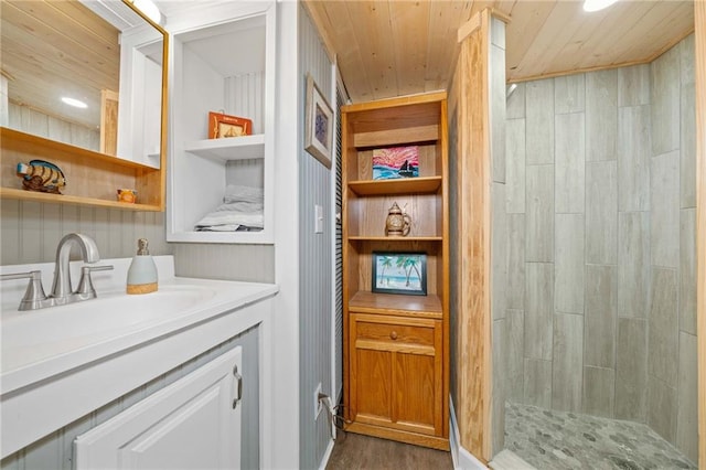 full bathroom with tiled shower, wood finished floors, wood ceiling, and vanity