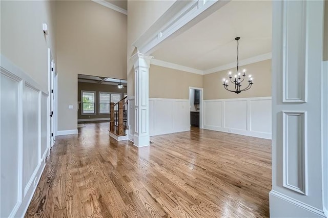 entryway featuring wood-type flooring, crown molding, ceiling fan with notable chandelier, and ornate columns