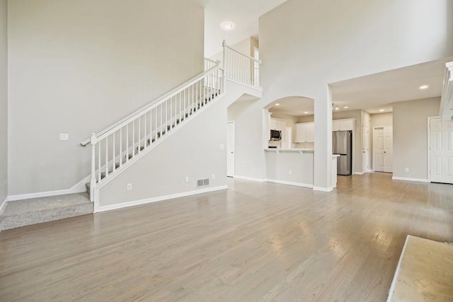 unfurnished living room with stairs, baseboards, visible vents, light wood-style floors, and a towering ceiling