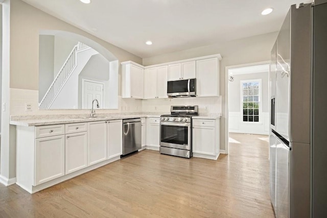 kitchen with a sink, light wood finished floors, white cabinetry, stainless steel appliances, and light stone countertops