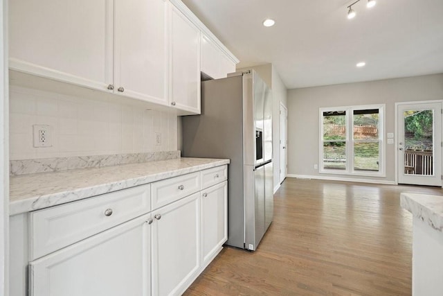 kitchen with light wood-style floors, light stone counters, white cabinets, and stainless steel fridge