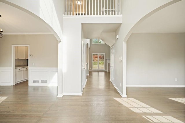 foyer with light wood-style flooring, crown molding, wainscoting, and a towering ceiling