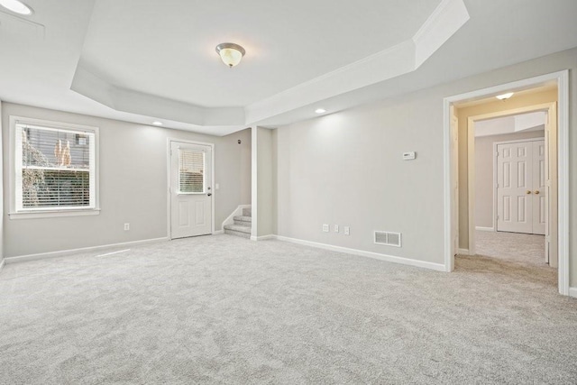 spare room with visible vents, light carpet, a tray ceiling, and stairway