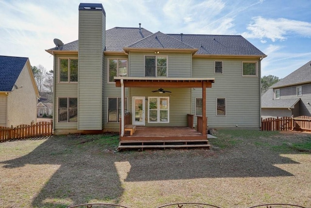 back of property with ceiling fan, a deck, a chimney, roof with shingles, and fence