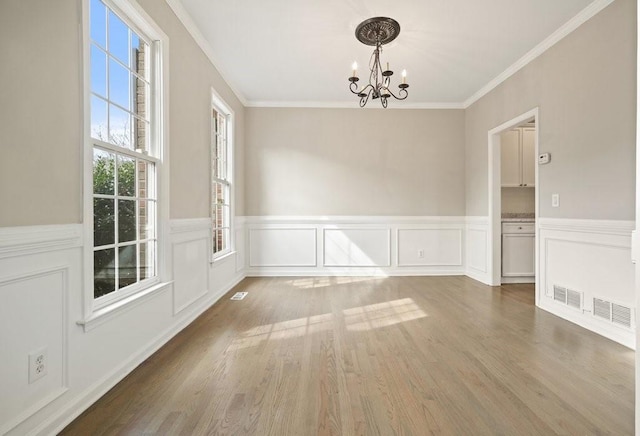 unfurnished dining area with crown molding, wood finished floors, an inviting chandelier, visible vents, and a wainscoted wall