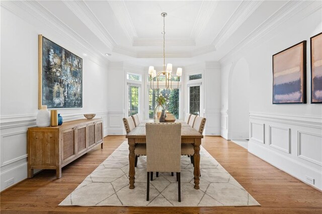 dining area with crown molding, light wood-type flooring, a notable chandelier, ornate columns, and a raised ceiling