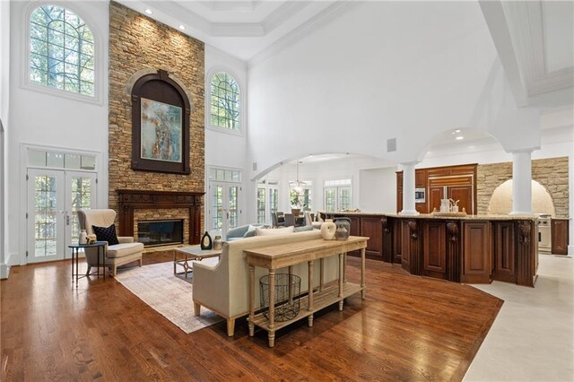 living room featuring french doors, a fireplace, a towering ceiling, decorative columns, and light hardwood / wood-style flooring