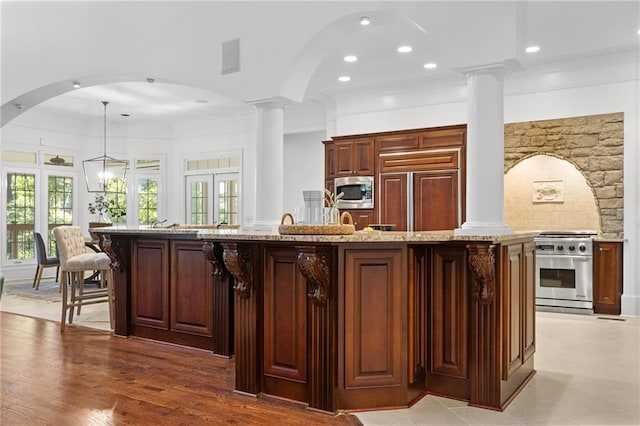 kitchen with stainless steel appliances, light hardwood / wood-style floors, light stone counters, hanging light fixtures, and an island with sink