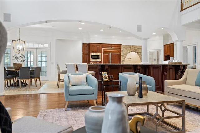 living room featuring a high ceiling, a chandelier, ornate columns, and light wood-type flooring