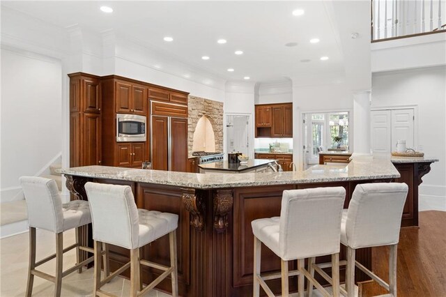 kitchen featuring a spacious island, built in appliances, light stone countertops, a kitchen breakfast bar, and light hardwood / wood-style flooring