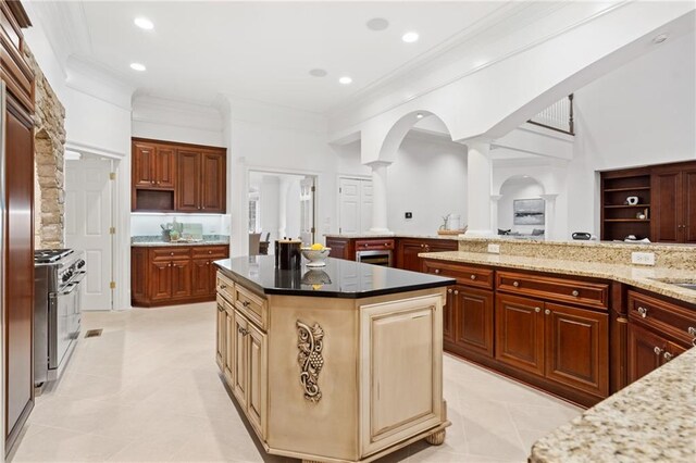 kitchen featuring dark stone counters, ornamental molding, stainless steel range, light tile patterned flooring, and a kitchen island