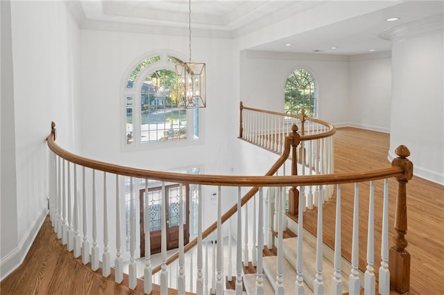 staircase with a chandelier, hardwood / wood-style flooring, ornamental molding, and plenty of natural light