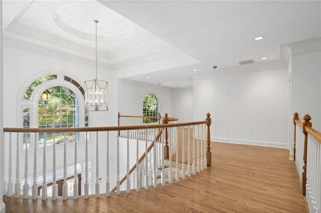 corridor with light wood-type flooring, a chandelier, crown molding, and a raised ceiling