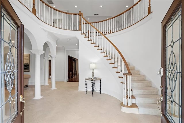 entryway featuring a towering ceiling, ornate columns, and crown molding