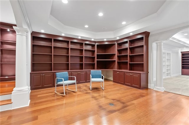 unfurnished room with built in shelves, a raised ceiling, ornamental molding, and light hardwood / wood-style flooring