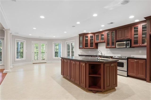 kitchen with crown molding, stove, sink, an island with sink, and decorative columns